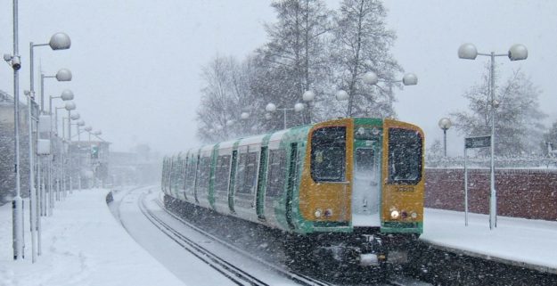 A green and yellow Southern train calls at a station in the snow, daytime