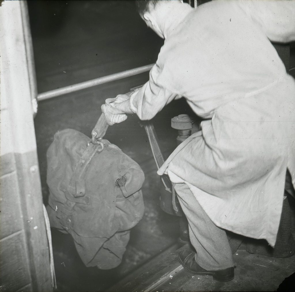 黑白照片传真照片的邮政工人降低的皮革袋邮件在铁路边的装置